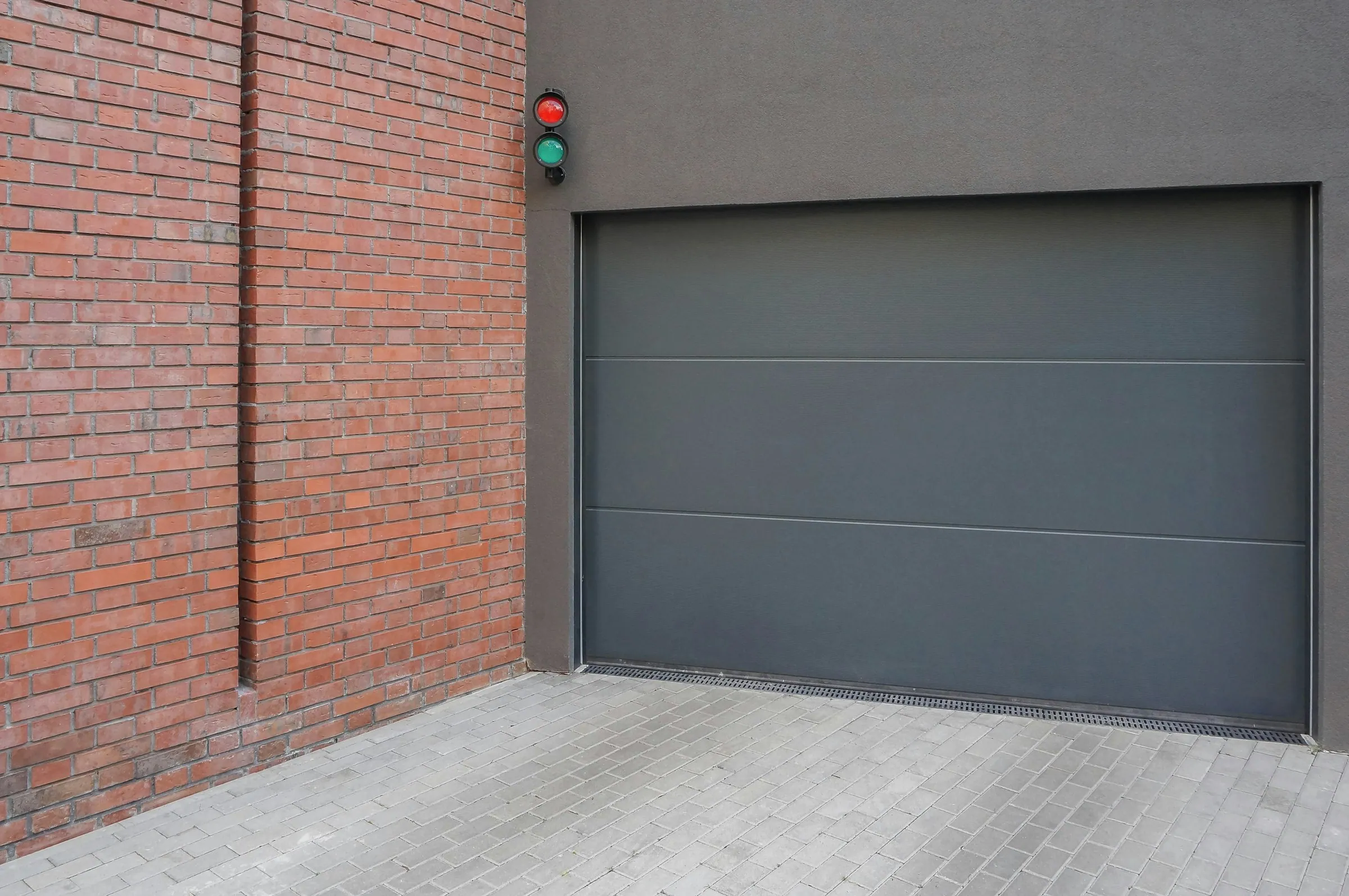 Grey aluminium sectional garage door beside a brick wall
