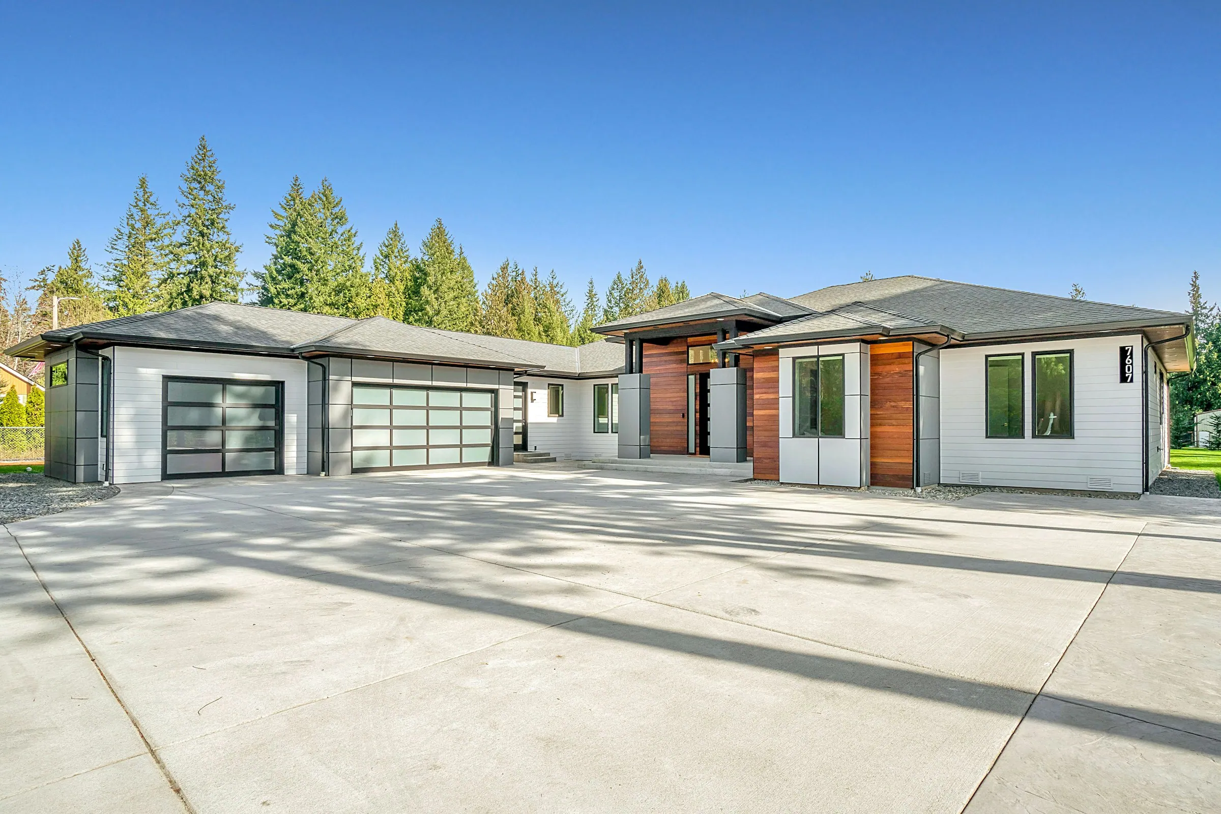 Suburban home with a driveway and mature trees under a blue sky